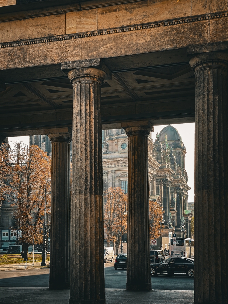 A close-up of columns of a building on Museum Island in Berlin, with a street with autumn leaves in the background
